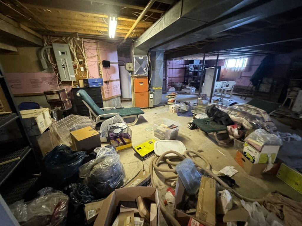 Basement junk including bags, boxes, a lounge chair and hoses waiting for removal