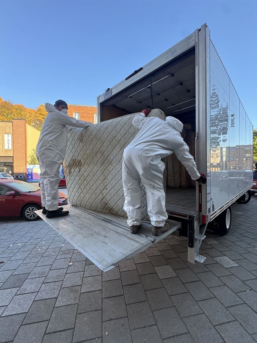 Crew in protective coveralls sliding a mattress into the junk removal truck