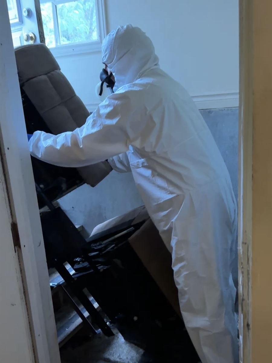 Crew member in protective gear removing items through a basement doorway
