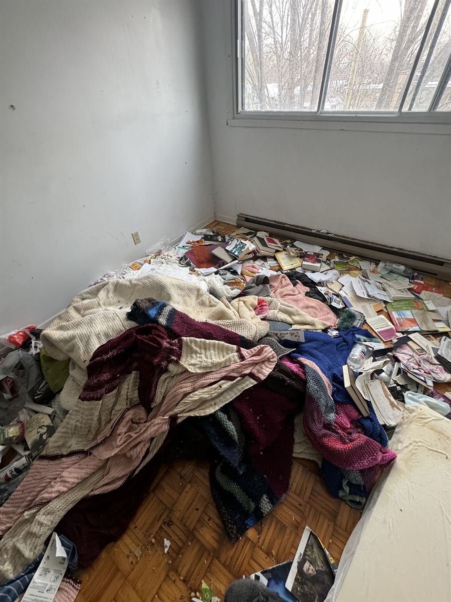 Bedroom floor covered in clothes and papers before a hoarding cleanup