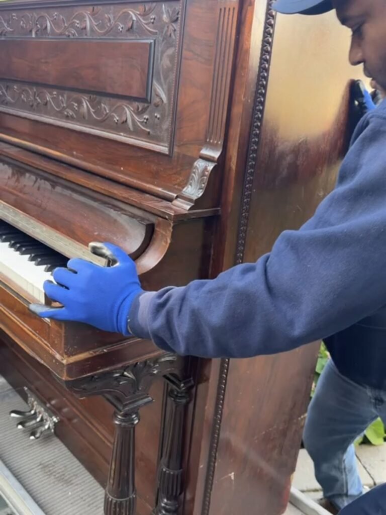 Crew member guiding an upright piano up the truck ramp