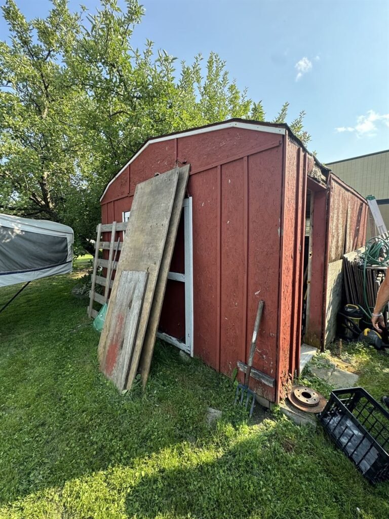 Old red wooden shed in a backyard before removal
